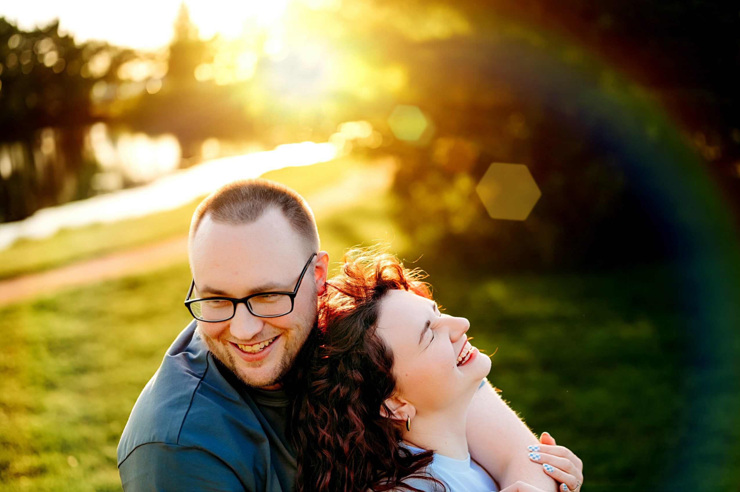 Two people smiling outdoors with sunlight and a rainbow in the background.