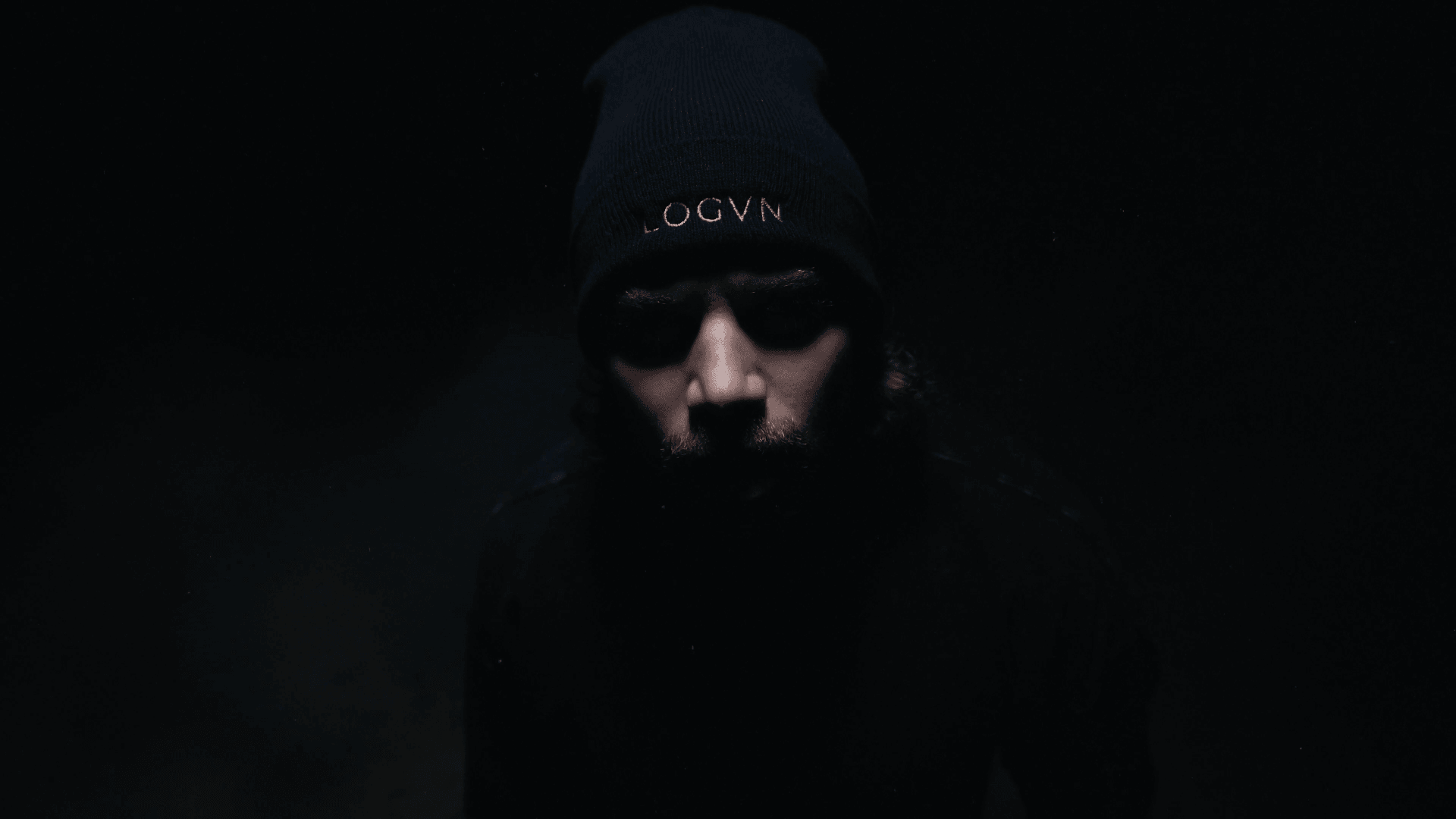 Person wearing a beanie with a dark background, face partially visible, low lighting.