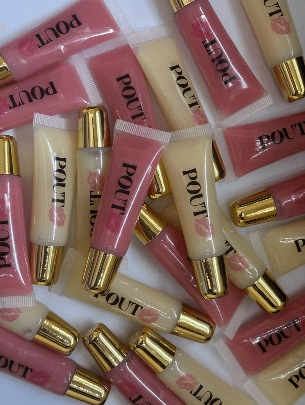 Multiple lip gloss tubes with pink and white shades, gold caps, and the word 'POUT' on the packaging.