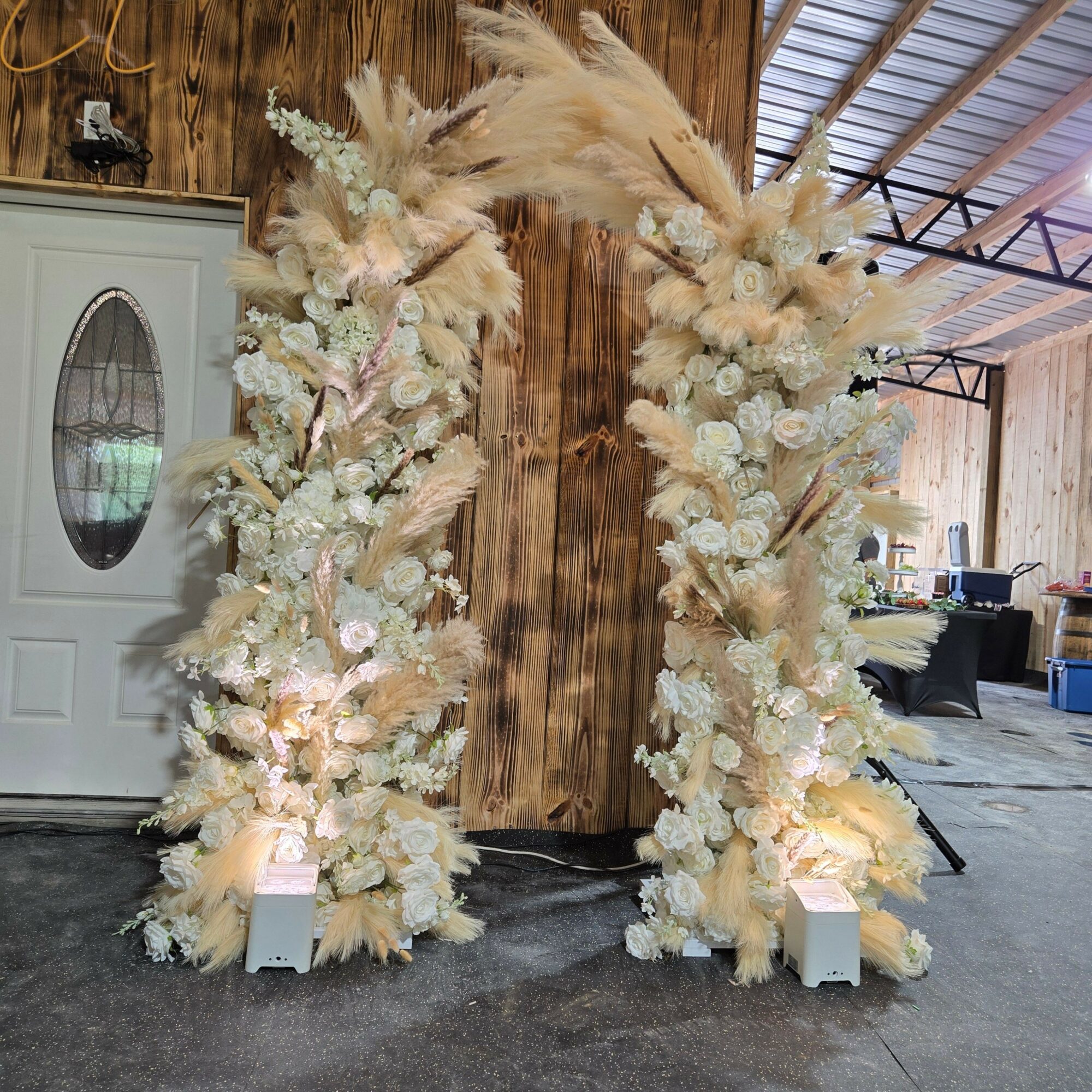 Decorative floral arrangement with white and cream-colored flowers and foliage, placed on a wooden surface indoors.
