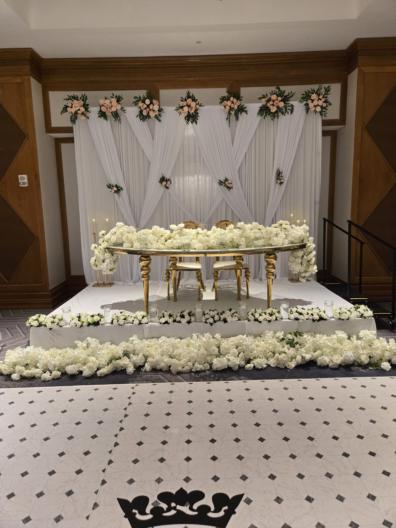 Elegant wedding setup with a floral backdrop, a long table decorated with white flowers, and a patterned floor.