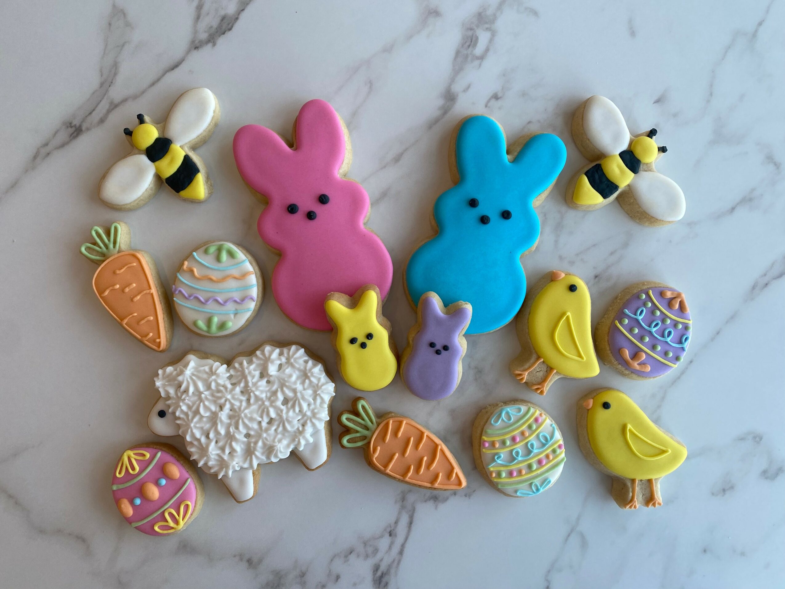 Colorful Easter-themed cookies and candies on a marble surface, including bunnies, chicks, eggs, carrots, and bees.