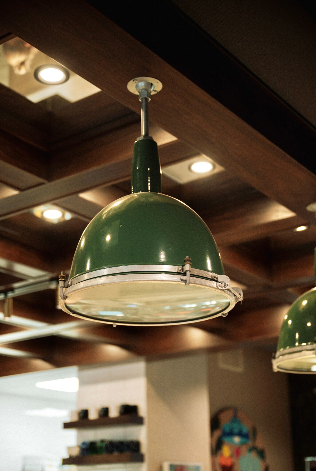 Green pendant light hanging from a ceiling with wooden beams, in a room with warm lighting.