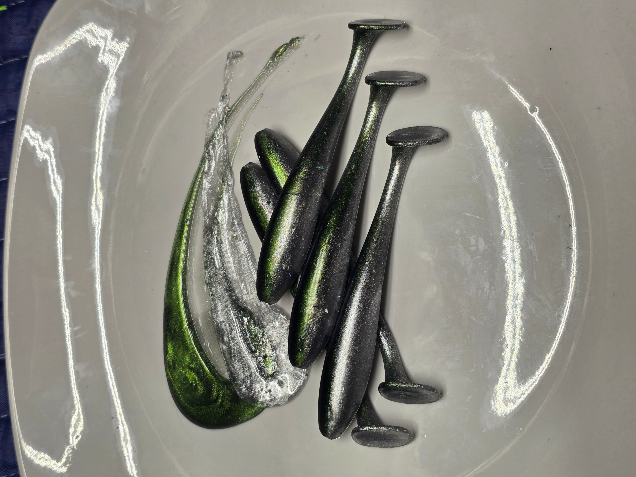 Six black and green golf tees inside a clear container, with a reflective surface and curved background.