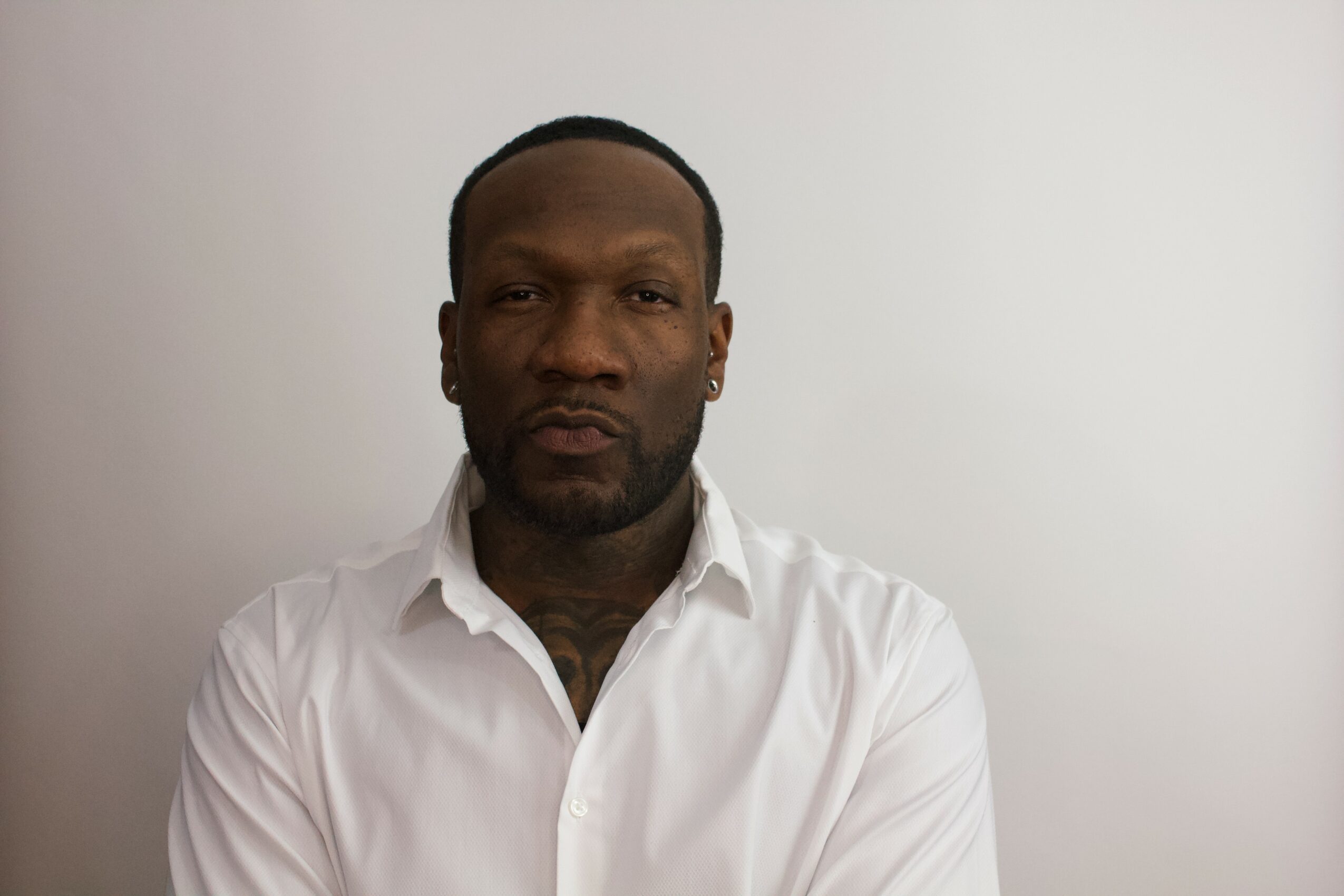 Man with short hair and beard wearing a white shirt against a plain background.