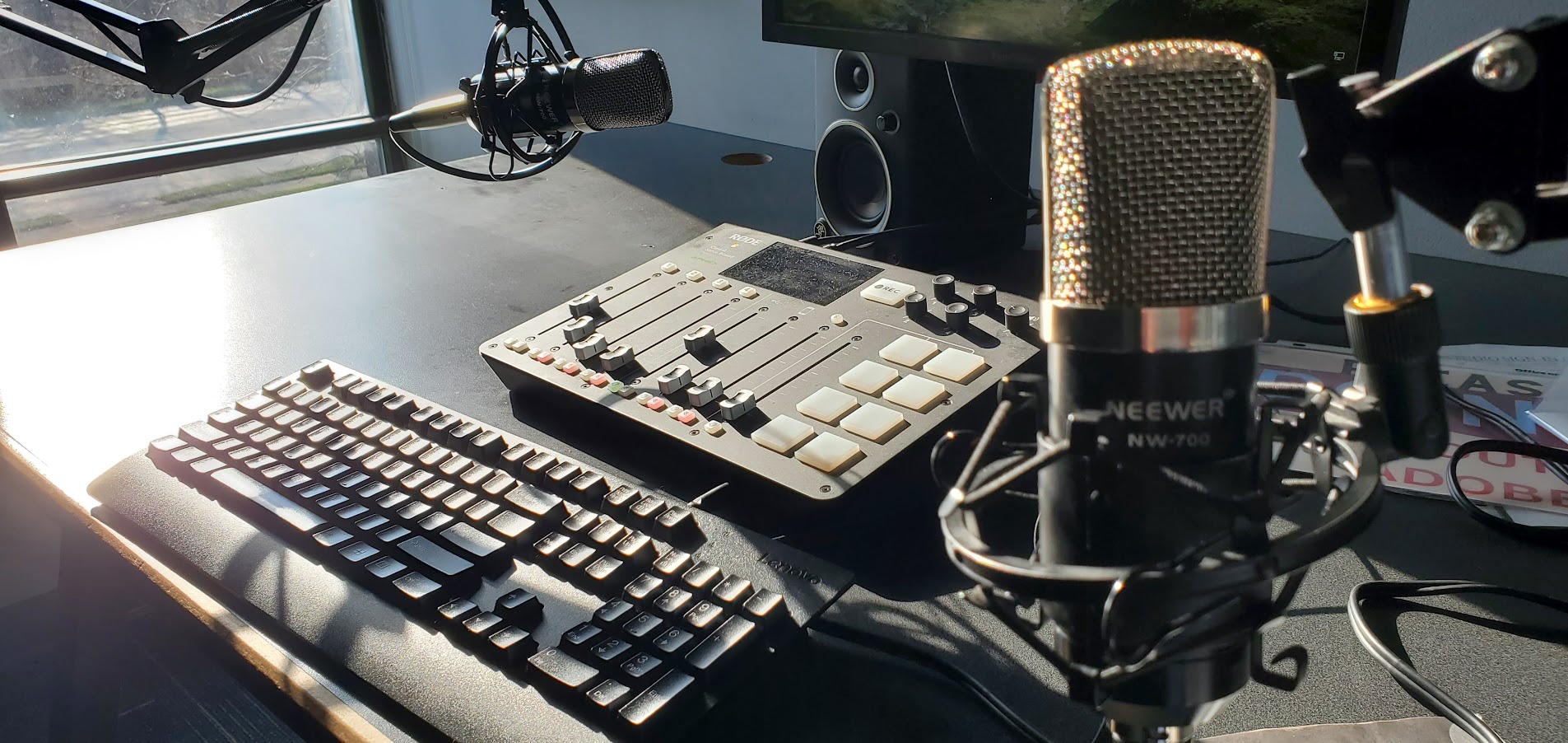 Computer keyboard, audio mixer, and microphone on a desk with sunlight shining on the surface.
