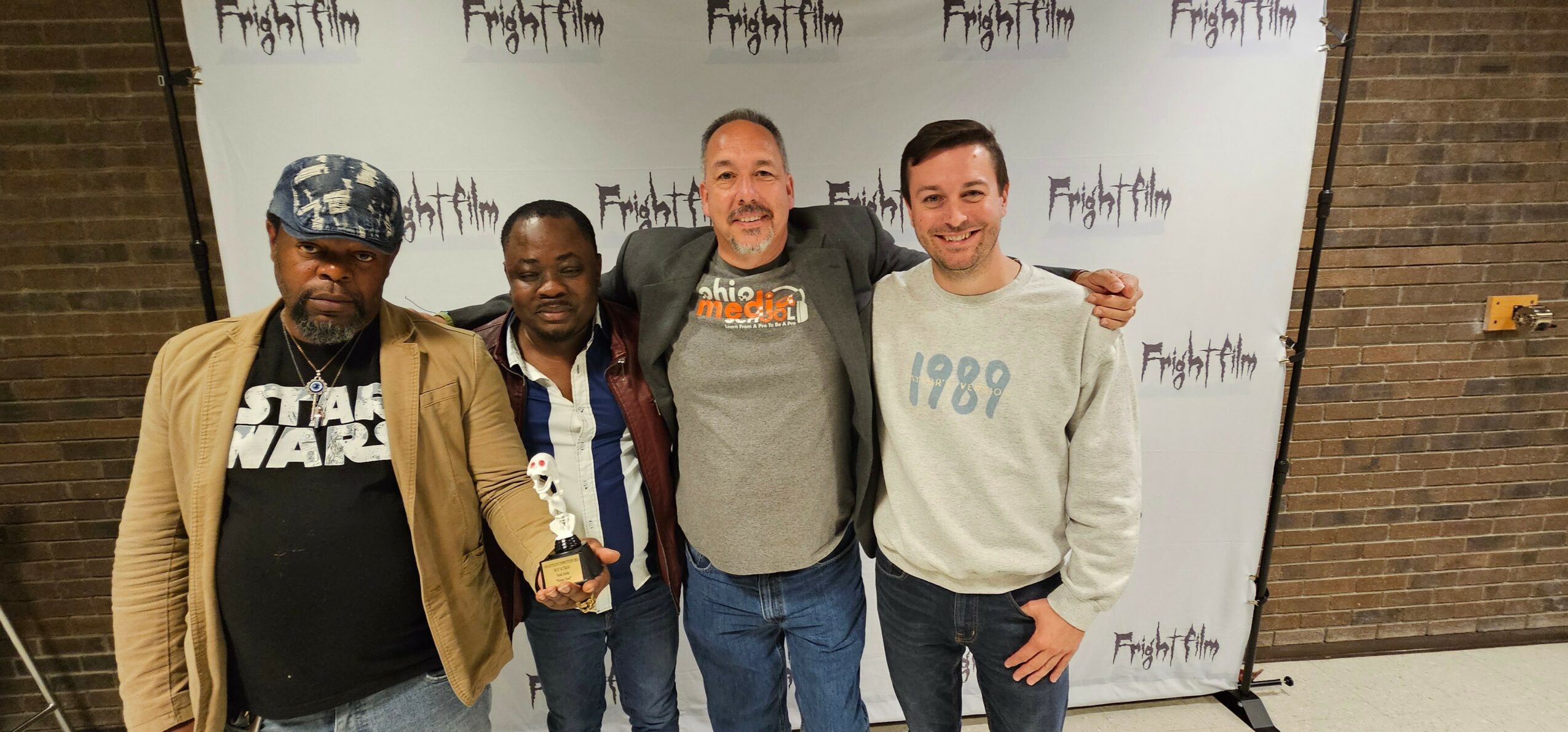 Four men standing together in front of a backdrop with text, smiling and posing for a photo.
