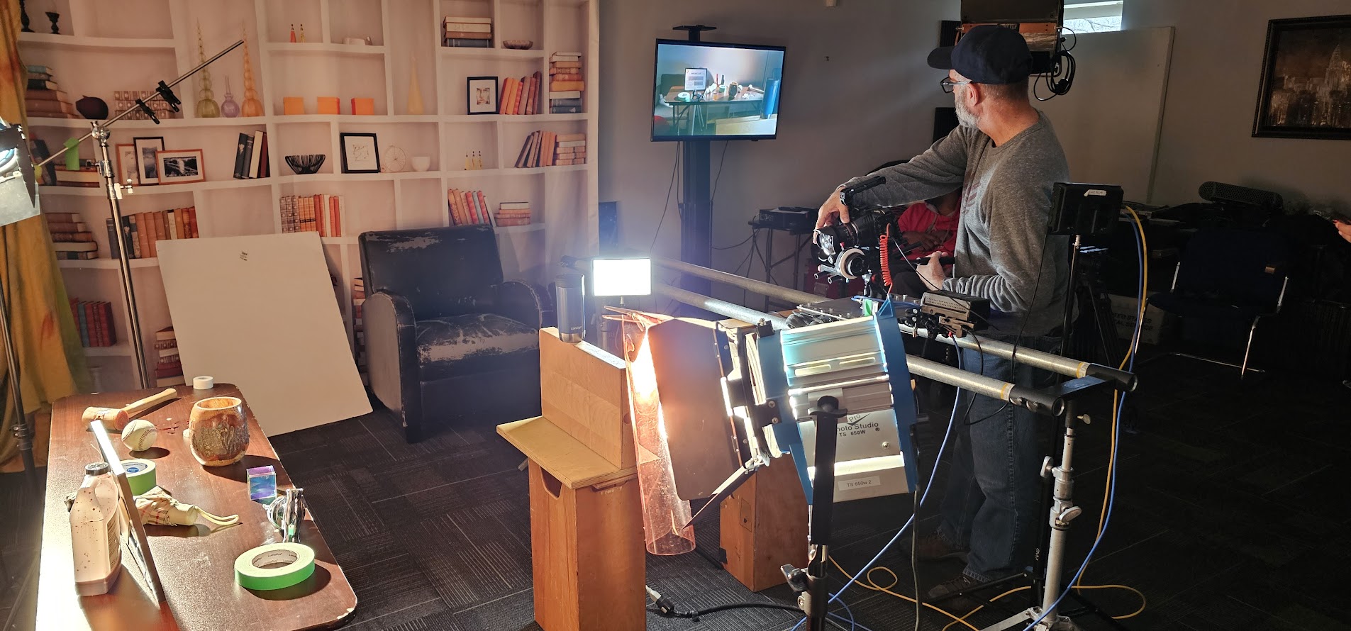 Person using virtual reality equipment in a room with various objects and a TV screen, illuminated by bright light.