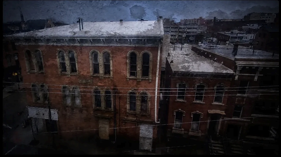 Snow-covered rooftops and buildings seen through a window during a storm, with raindrops on the glass.
