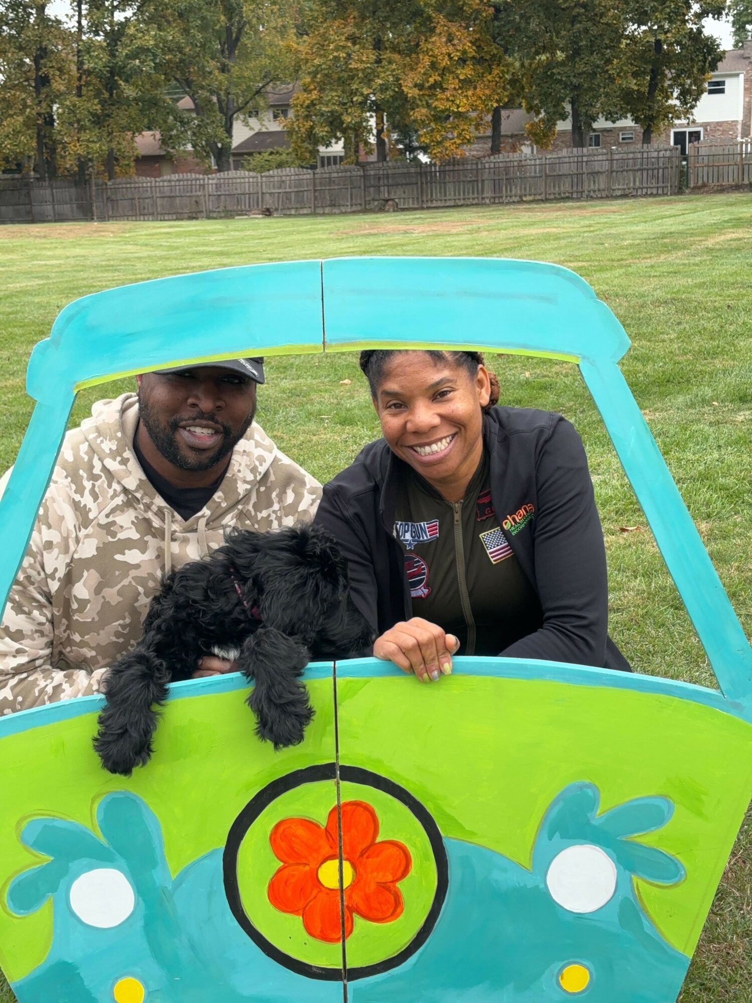 Two women leaning on a colorful, cartoon-themed table outdoors, smiling at the camera, with grass and trees in the background.