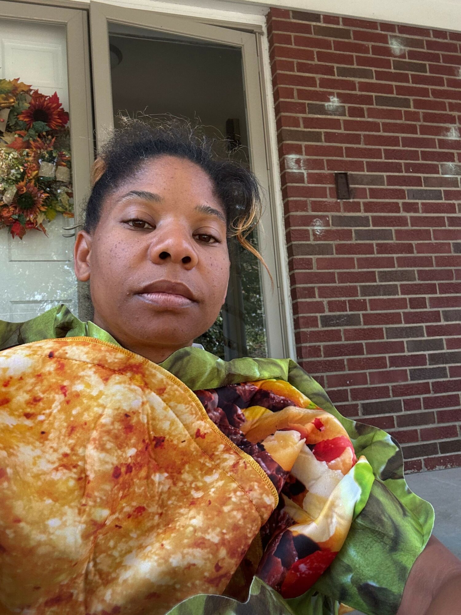 Woman holding a pizza slice and a salad outside a house with a brick wall and window, flowers visible inside.