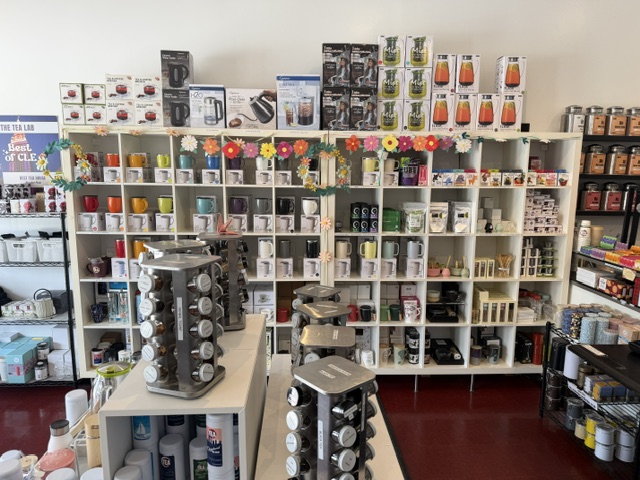 Display shelves filled with various kitchenware and household items, with a table holding rotating spice racks in front.