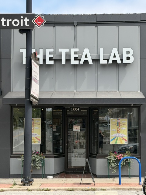 storefront with sign reading 'THE TEA LAB', glass door entrance, two flower pots, and a blue bike rack outside