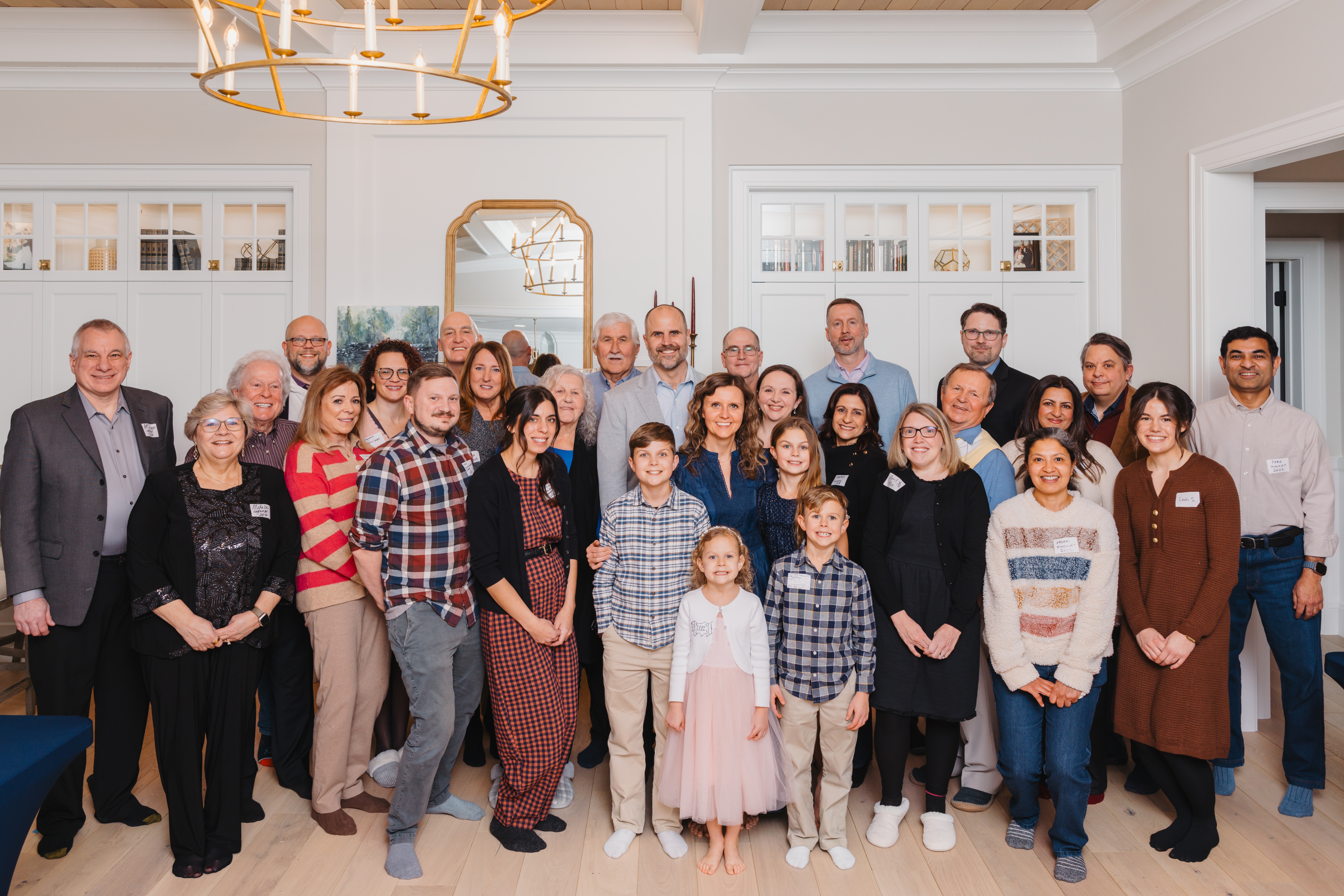 Group of adults and children gathered in a bright, elegant room with white walls and a gold chandelier.