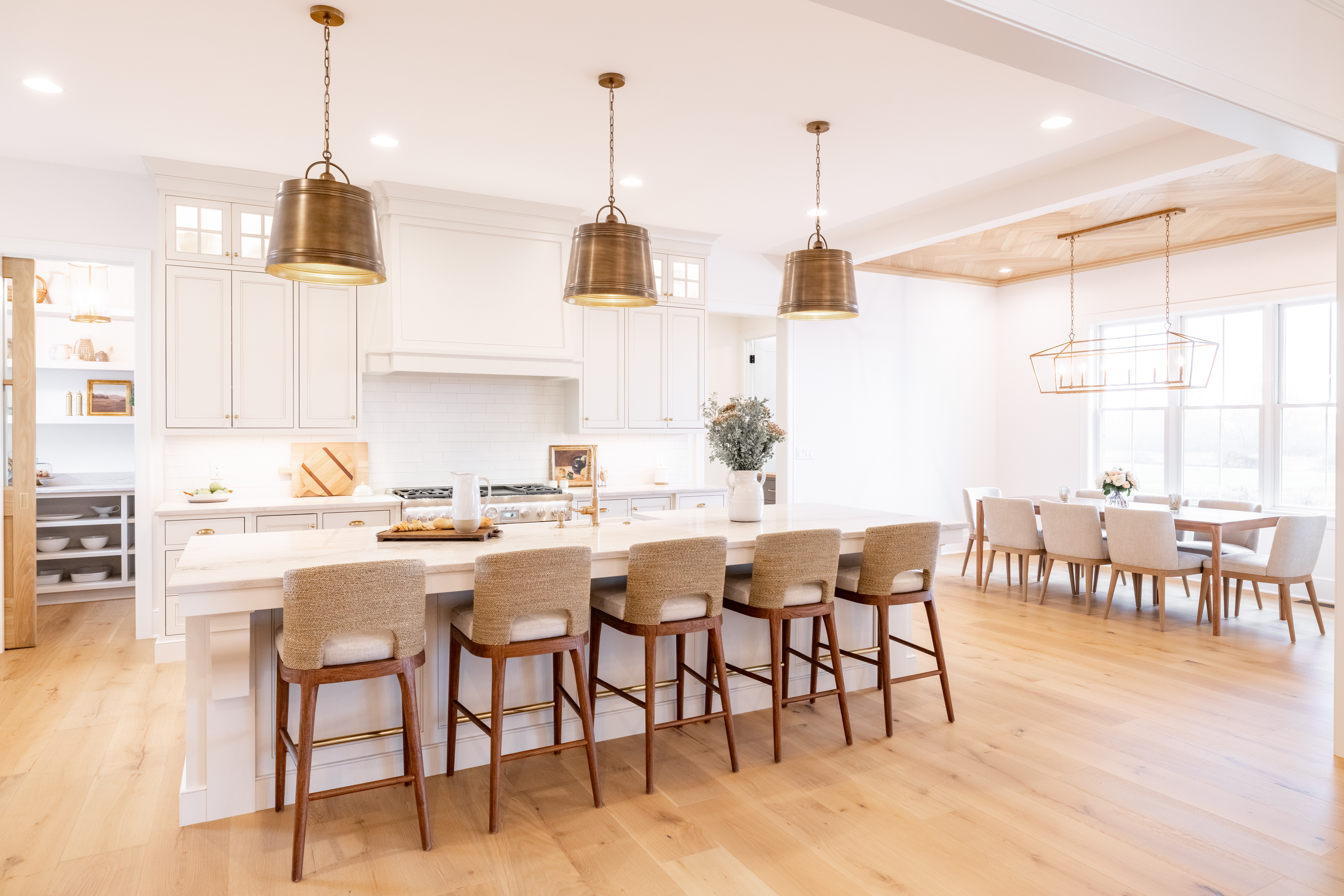 Bright kitchen with white cabinets, a large island with six chairs, pendant lights, and a dining area with a table and chairs.