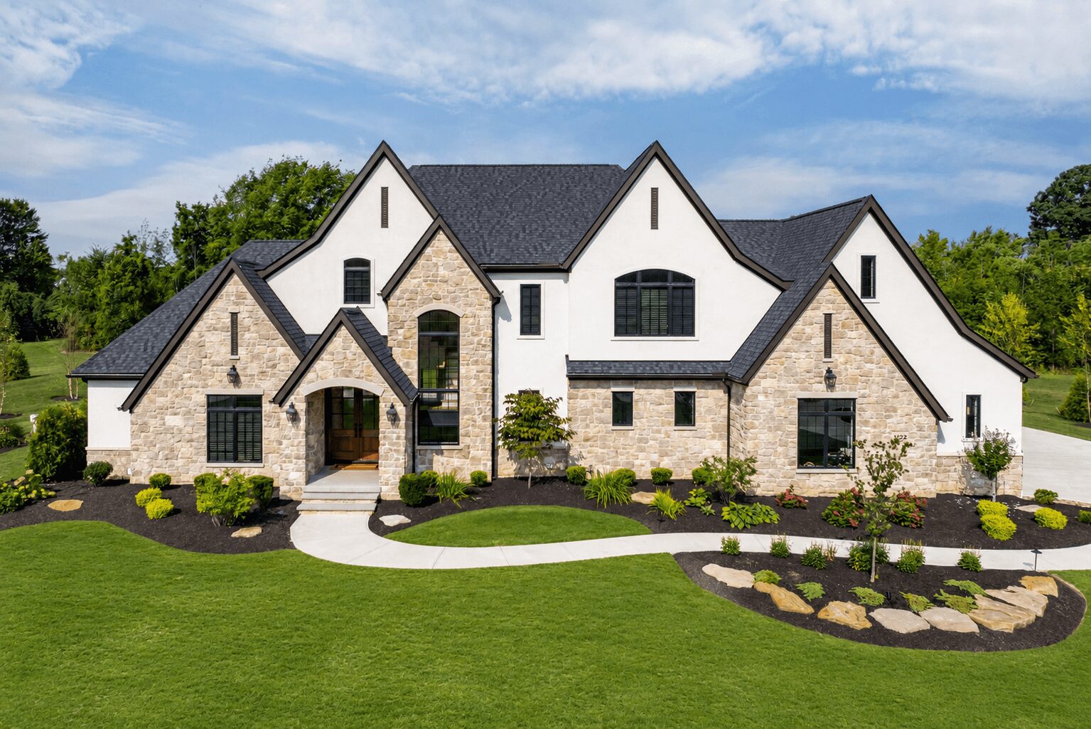 Large house with stone and white exterior, multiple gabled roofs, surrounded by green lawn and landscaping.