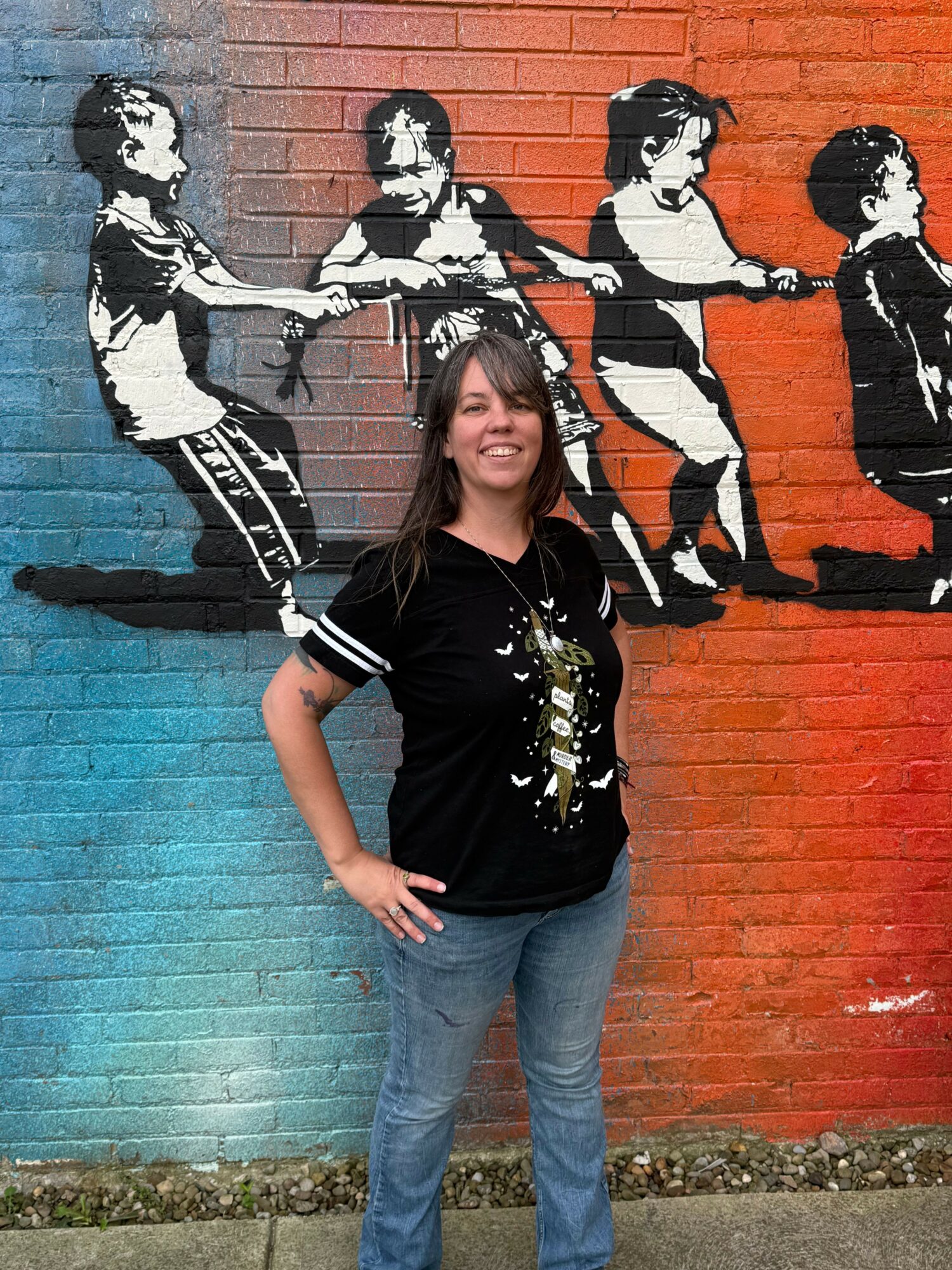 Person standing in front of a mural of four people playing musical instruments on a red and blue wall.