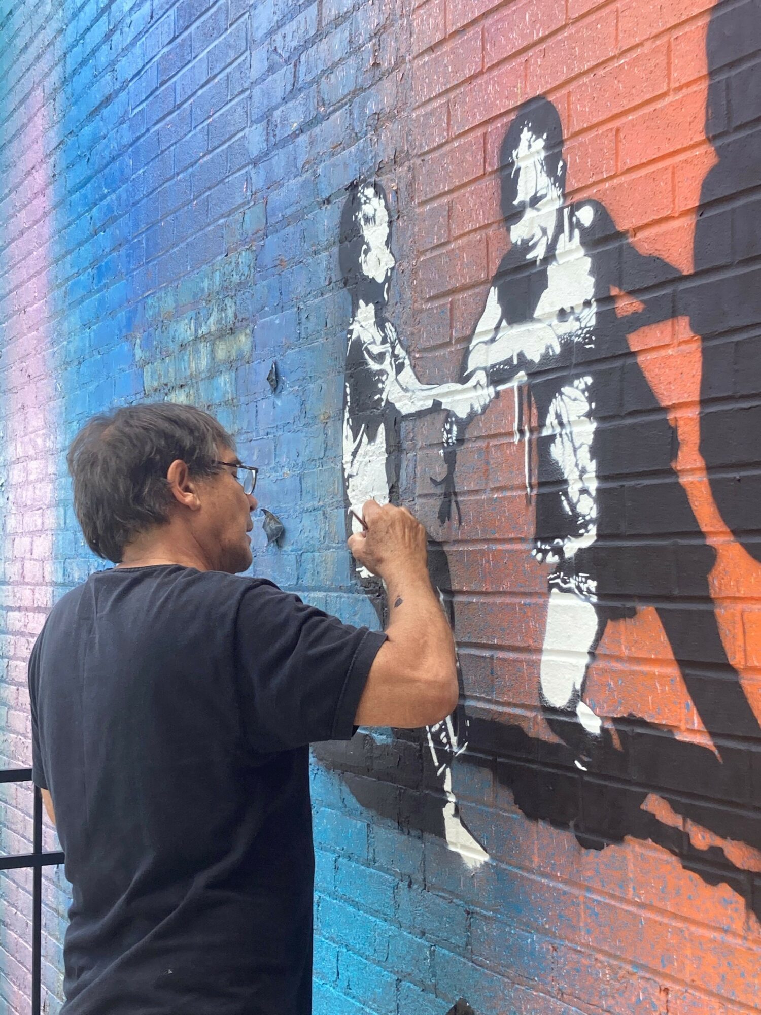 Person with short hair and black shirt standing in front of a colorful mural, looking at the artwork.
