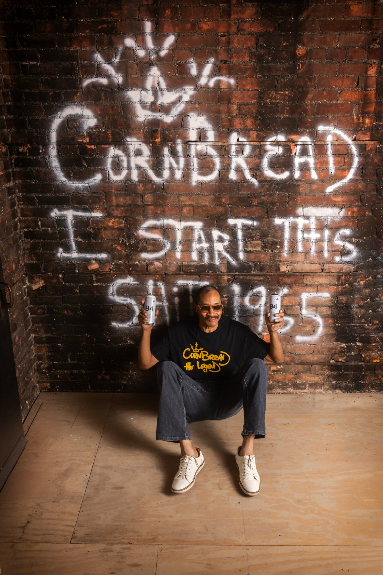 Person sitting on floor in front of graffiti reading 'Cornbread I start this shit 95.5'.