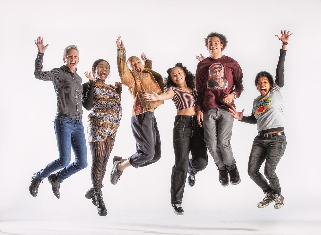 Group of six people jumping with arms raised, smiling, against a white background.