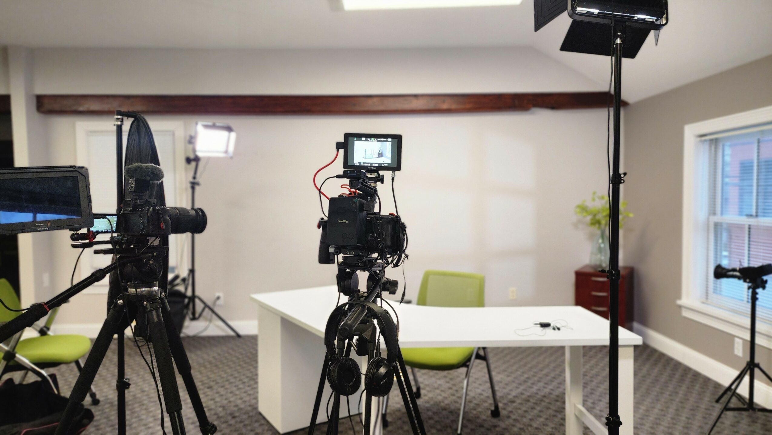 Video production setup with cameras, lights, and a table in a room with windows and a plant.