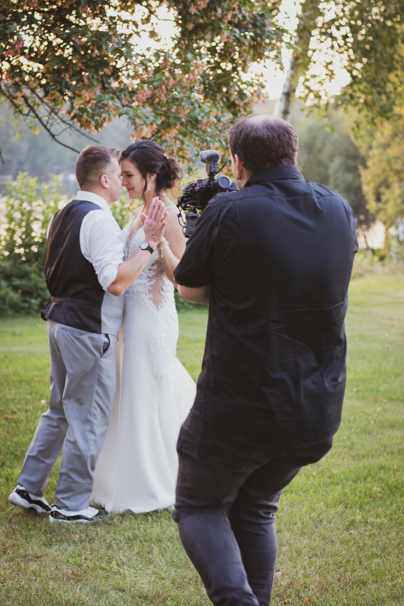 Photographer capturing a wedding scene with a bride, two young boys, and a man outdoors in a park-like setting.