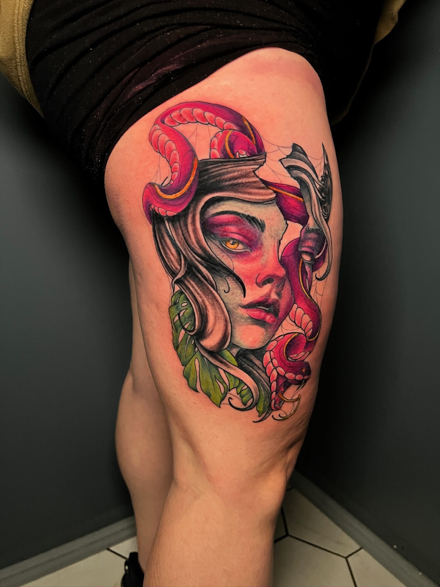 Tattoo of a woman with snake hair, horns, and colorful details on thigh, with leaves and vibrant colors.