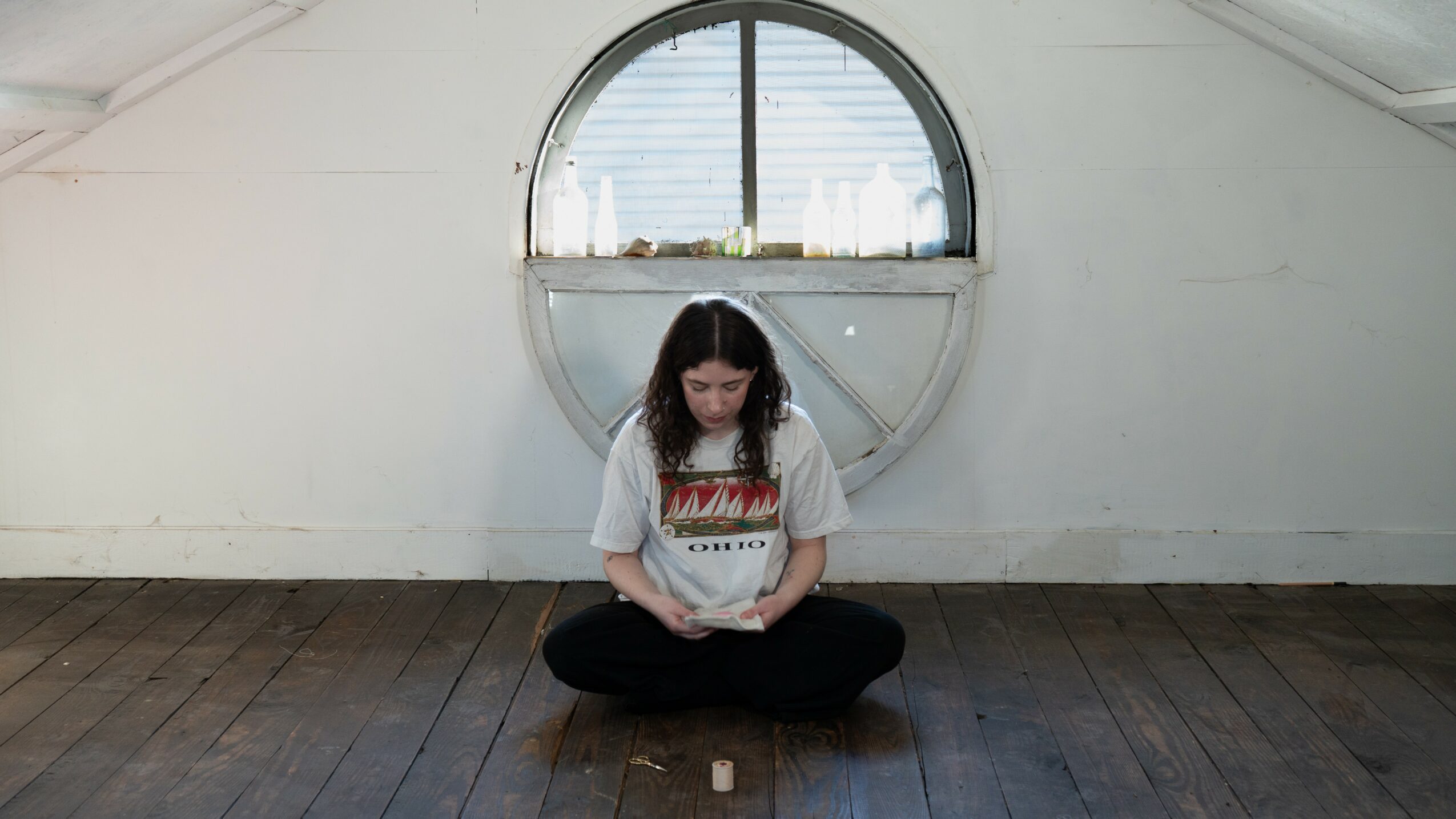 Person sitting cross-legged on wooden floor in front of a circular window with cityscape view.