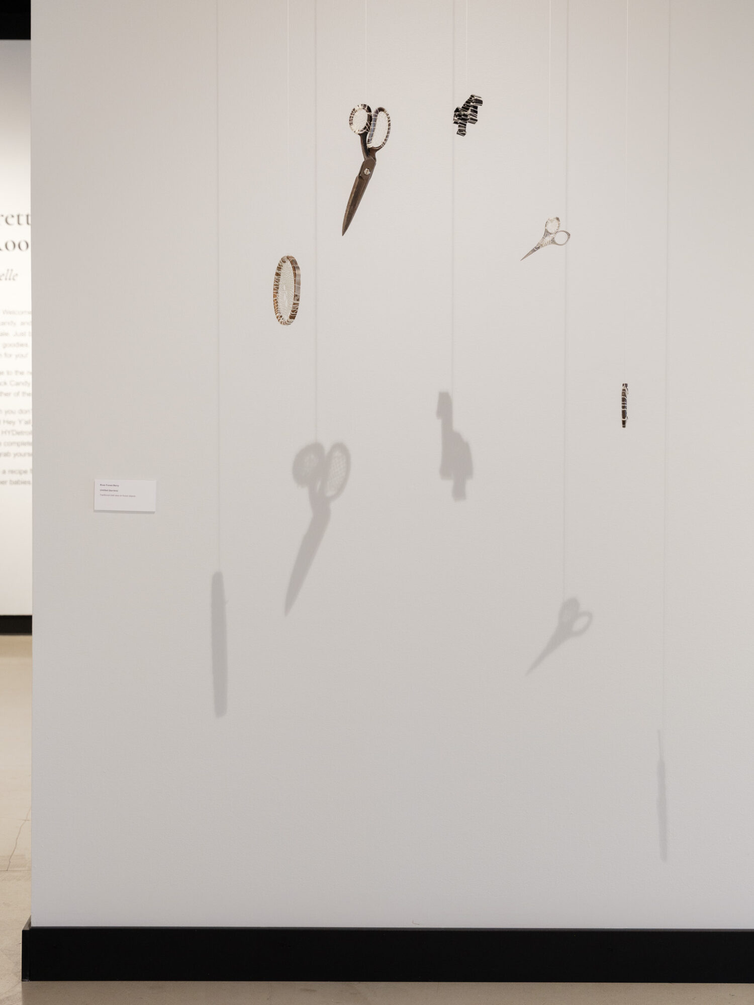 Wall with hanging objects including scissors, rings, and small items, casting shadows on a plain white background.