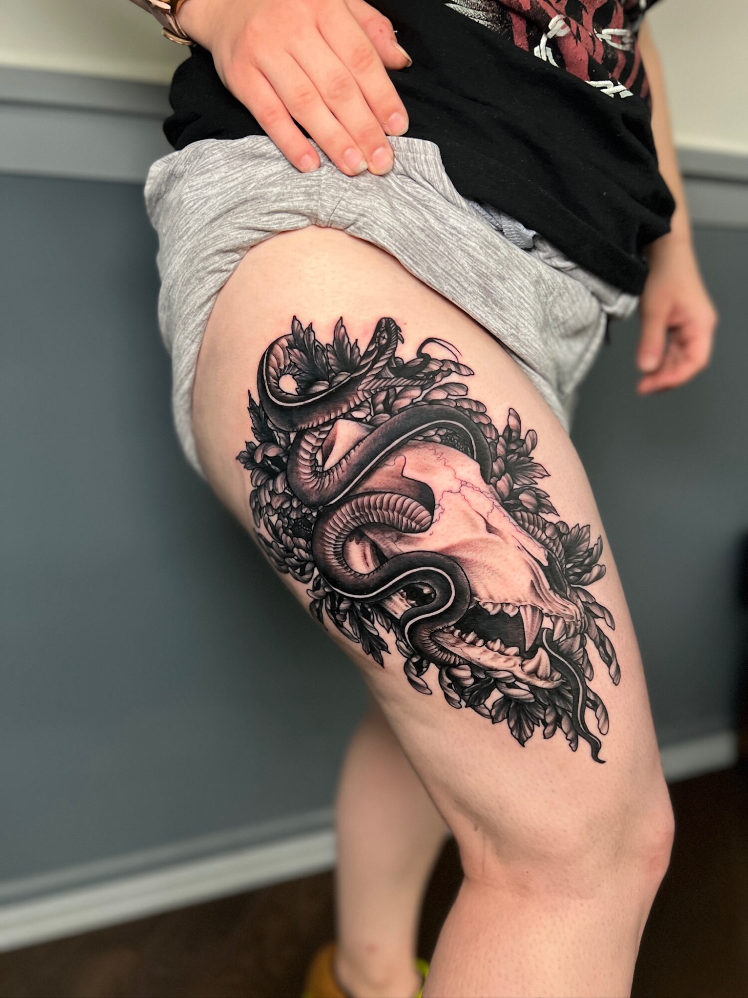 Person with a detailed black and gray dragon tattoo on their thigh, wearing gray shorts and a black shirt.