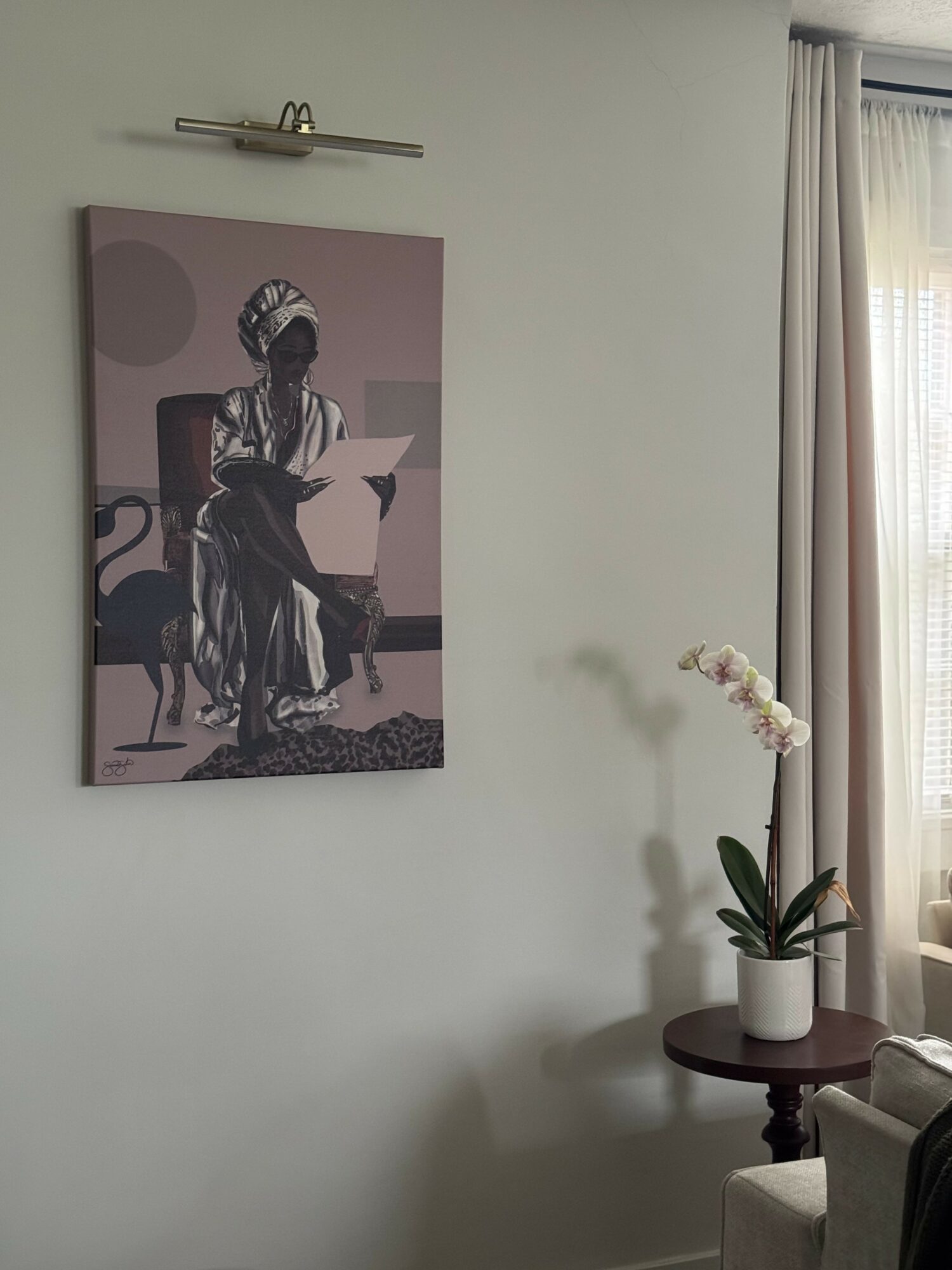 Wall with framed artwork, potted orchid on small table, and window with curtains.