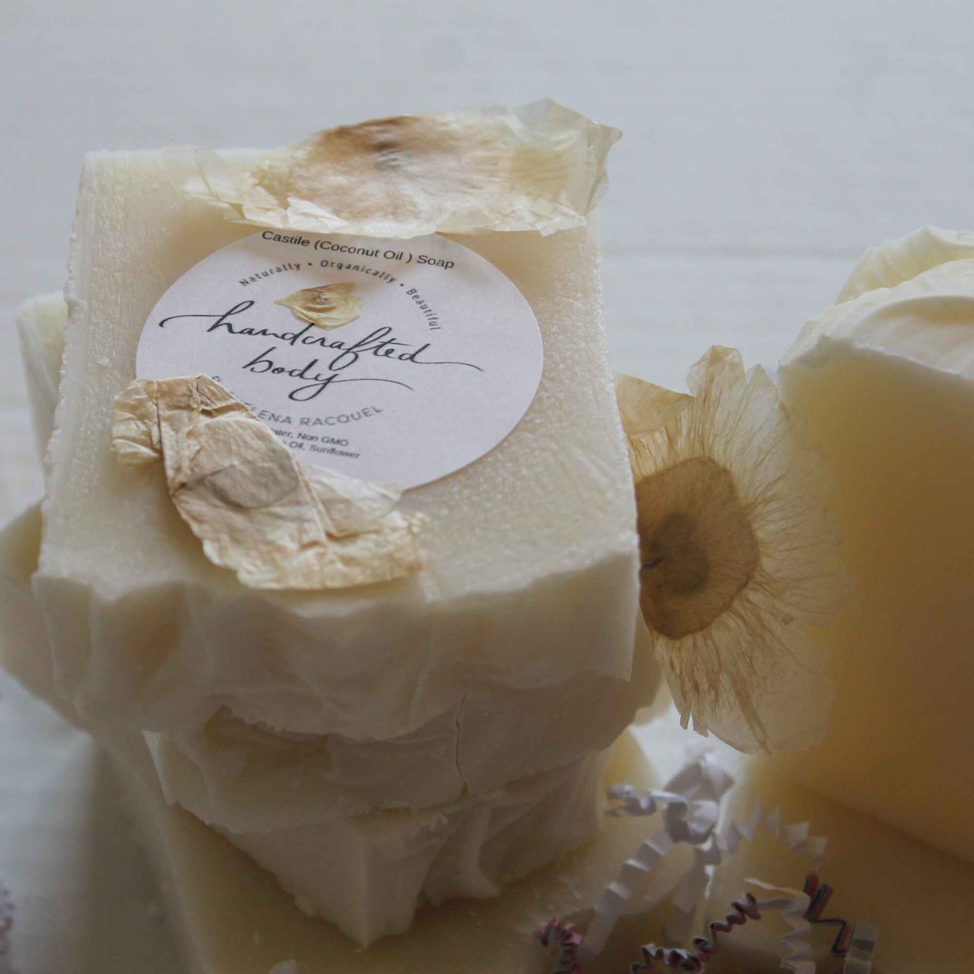 Cream-colored soap with a label, surrounded by flower petals and a flower, on a light background.