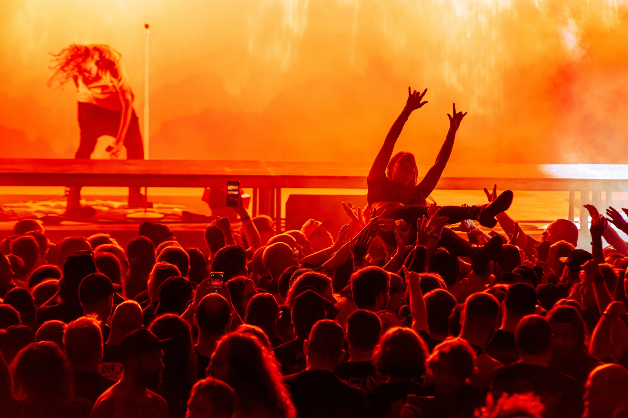 Crowd at concert with person crowd surfing, orange stage lighting, and smoke in background.