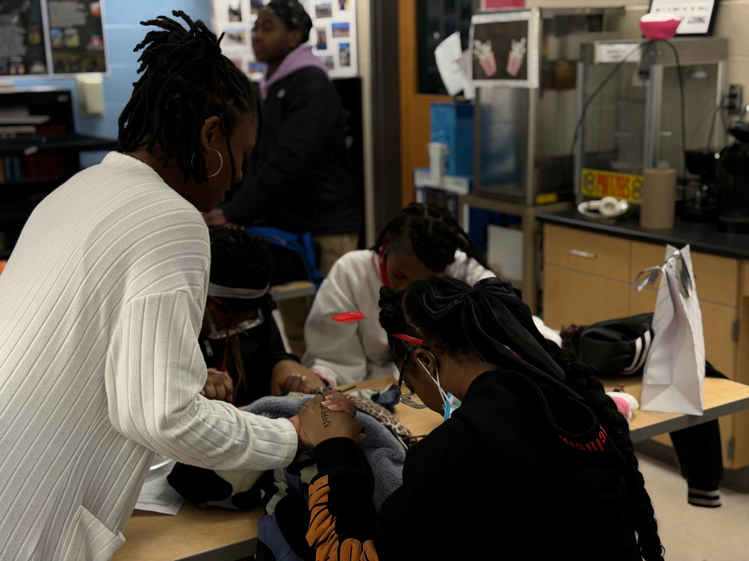 People gathered around a table in a room with shelves and equipment, engaging in an activity together.