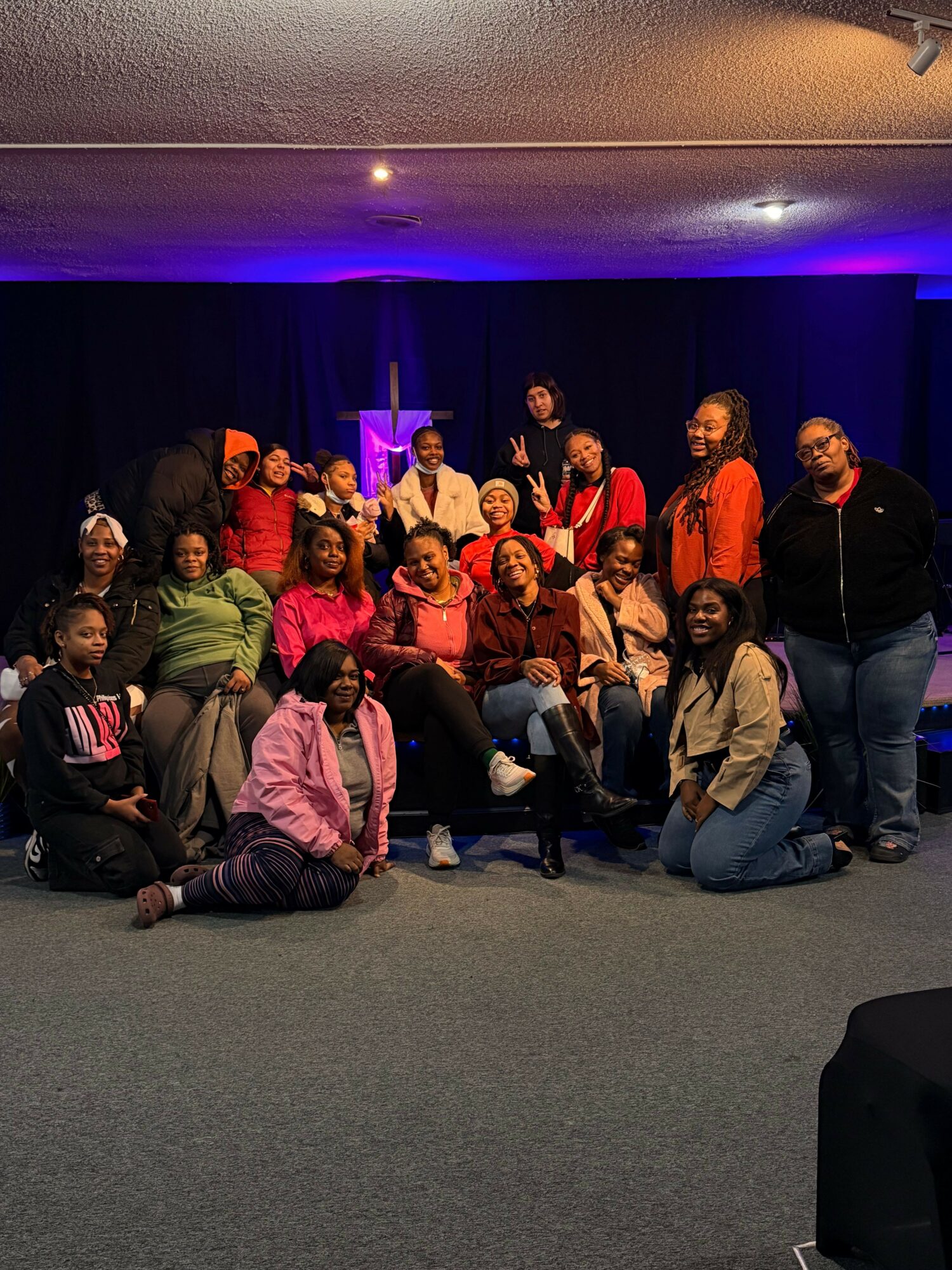 Group of people sitting and standing on a stage with purple lighting, posing for a photo.