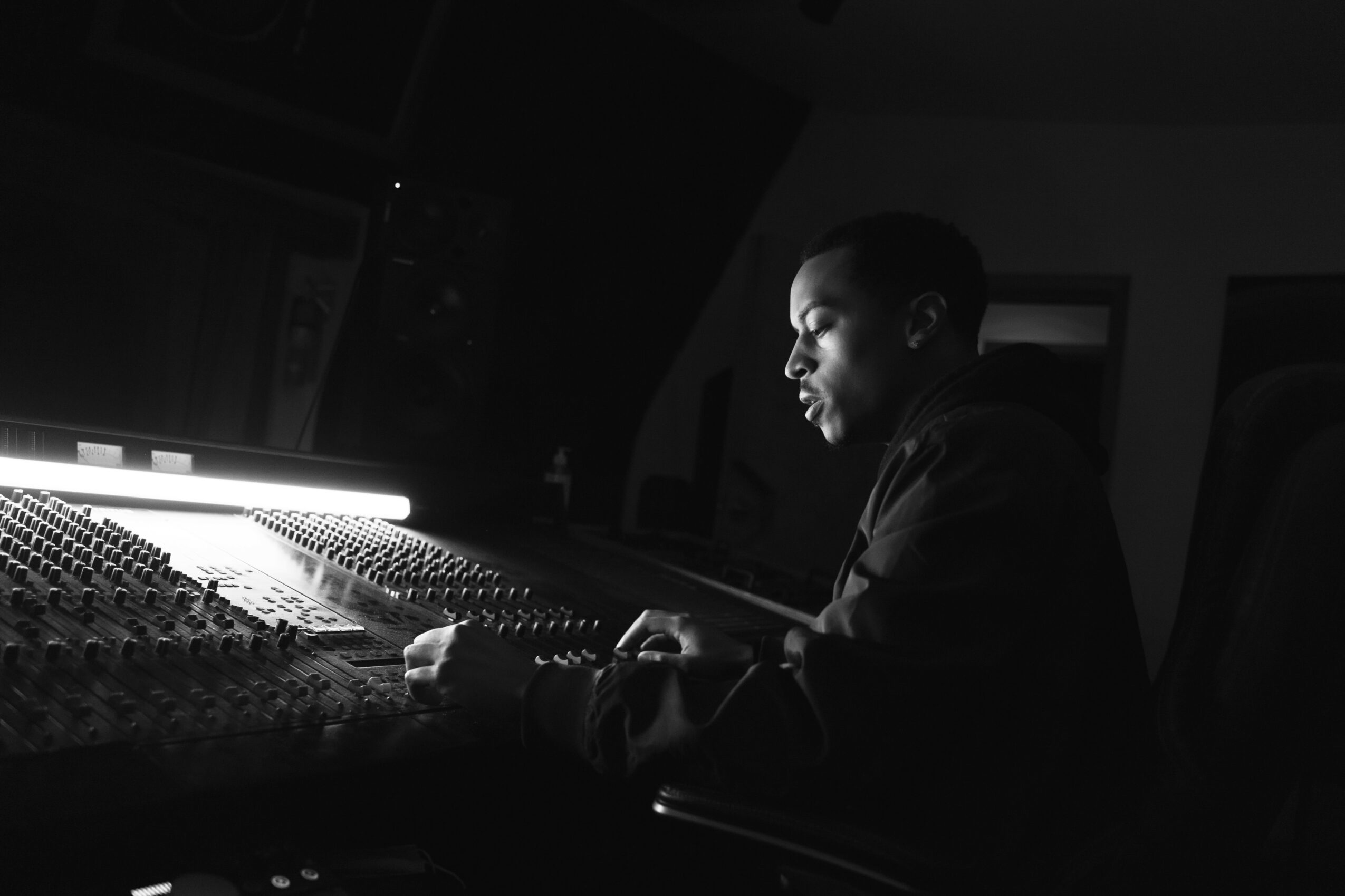 Person working at a mixing console in a dimly lit room, illuminated by a bright light, focused on the controls.
