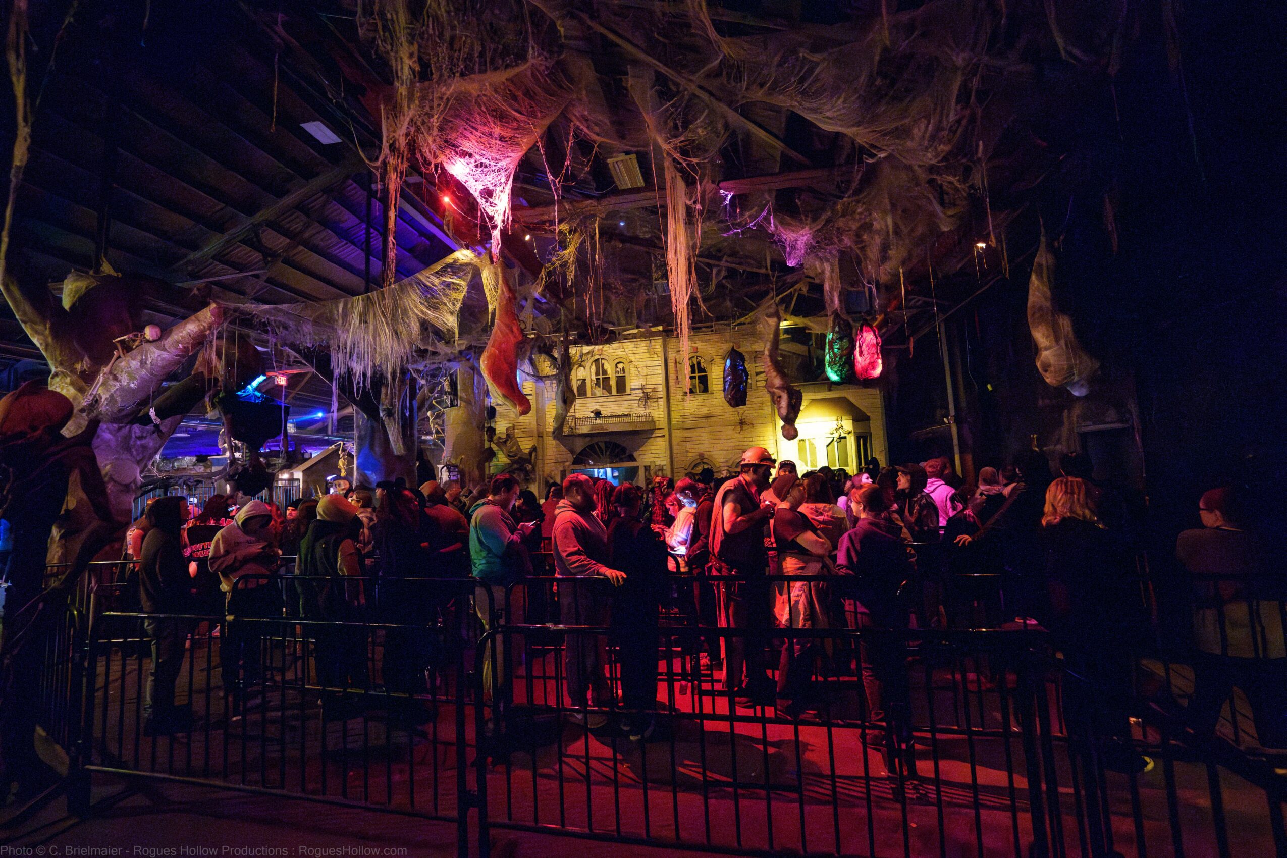 Crowd gathered in a dark, colorful indoor space with hanging decorations and vibrant lighting.