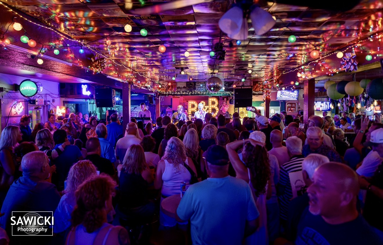 Crowd of people watching a performance on stage with colorful lights and decorations overhead.