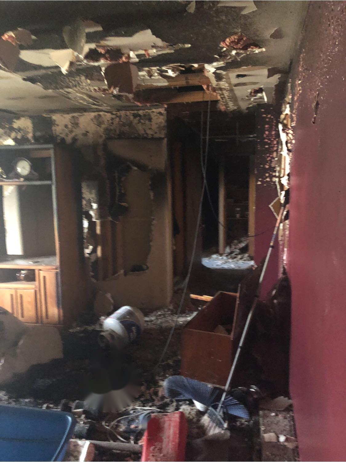 Room with damaged walls, burnt furniture, and debris scattered across the floor.