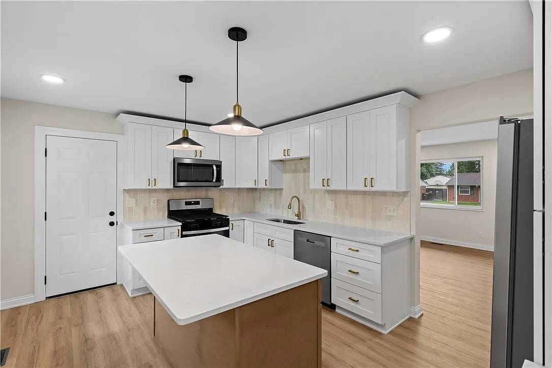 Modern kitchen with white cabinets, island, black appliances, and wood flooring, bright and spacious with a window view.