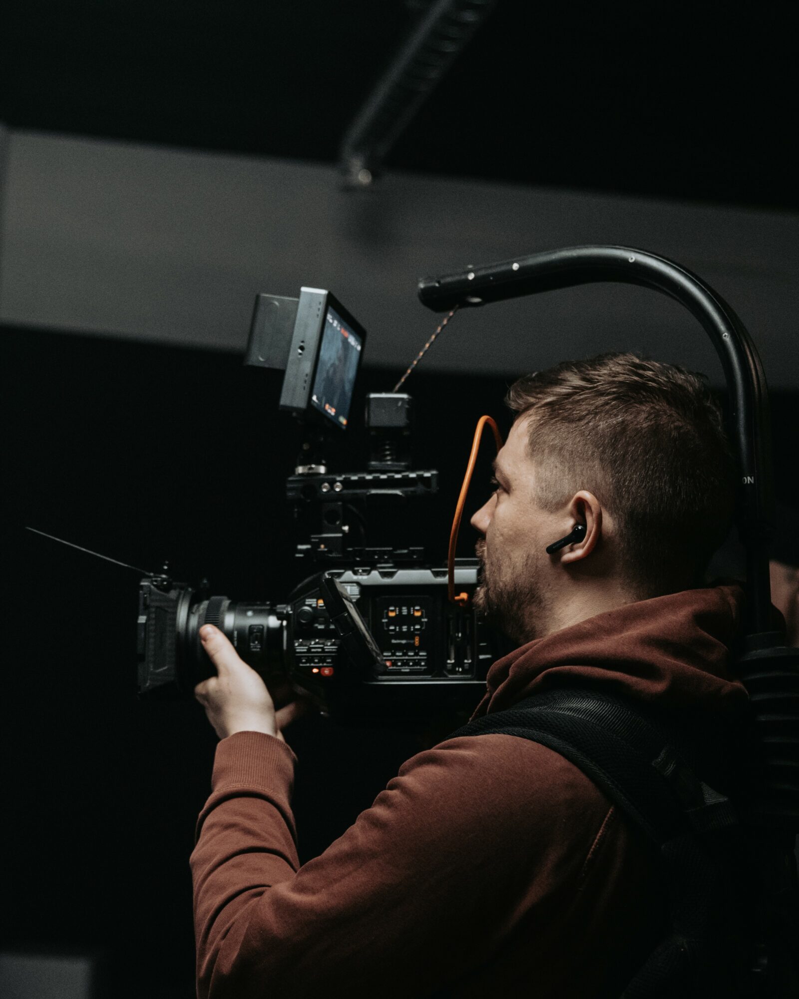 Person operating a professional video camera in a dark room, with equipment mounted on their shoulder.