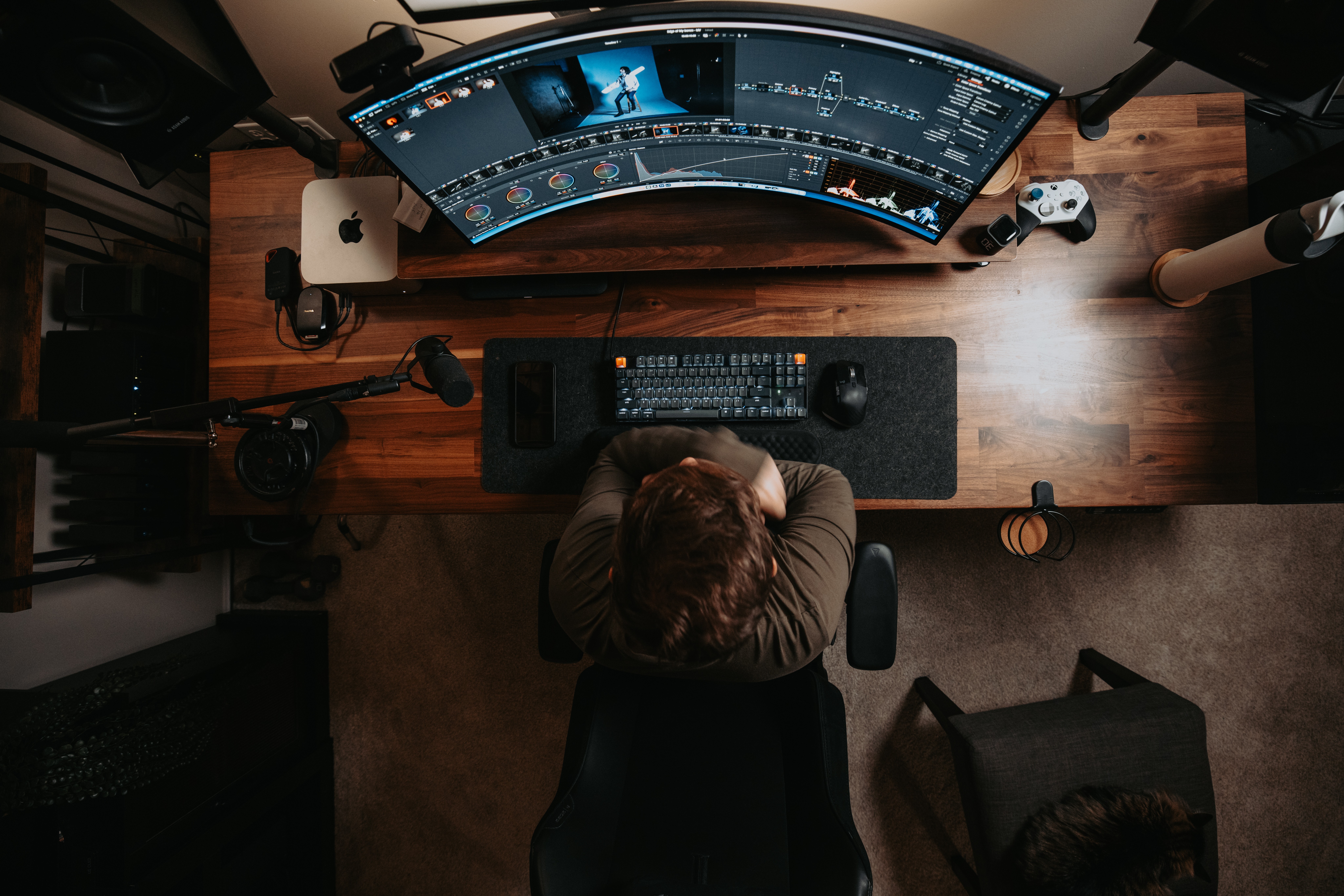 Person sitting at a desk with a curved monitor displaying a digital interface, keyboard, and mouse, viewed from above.