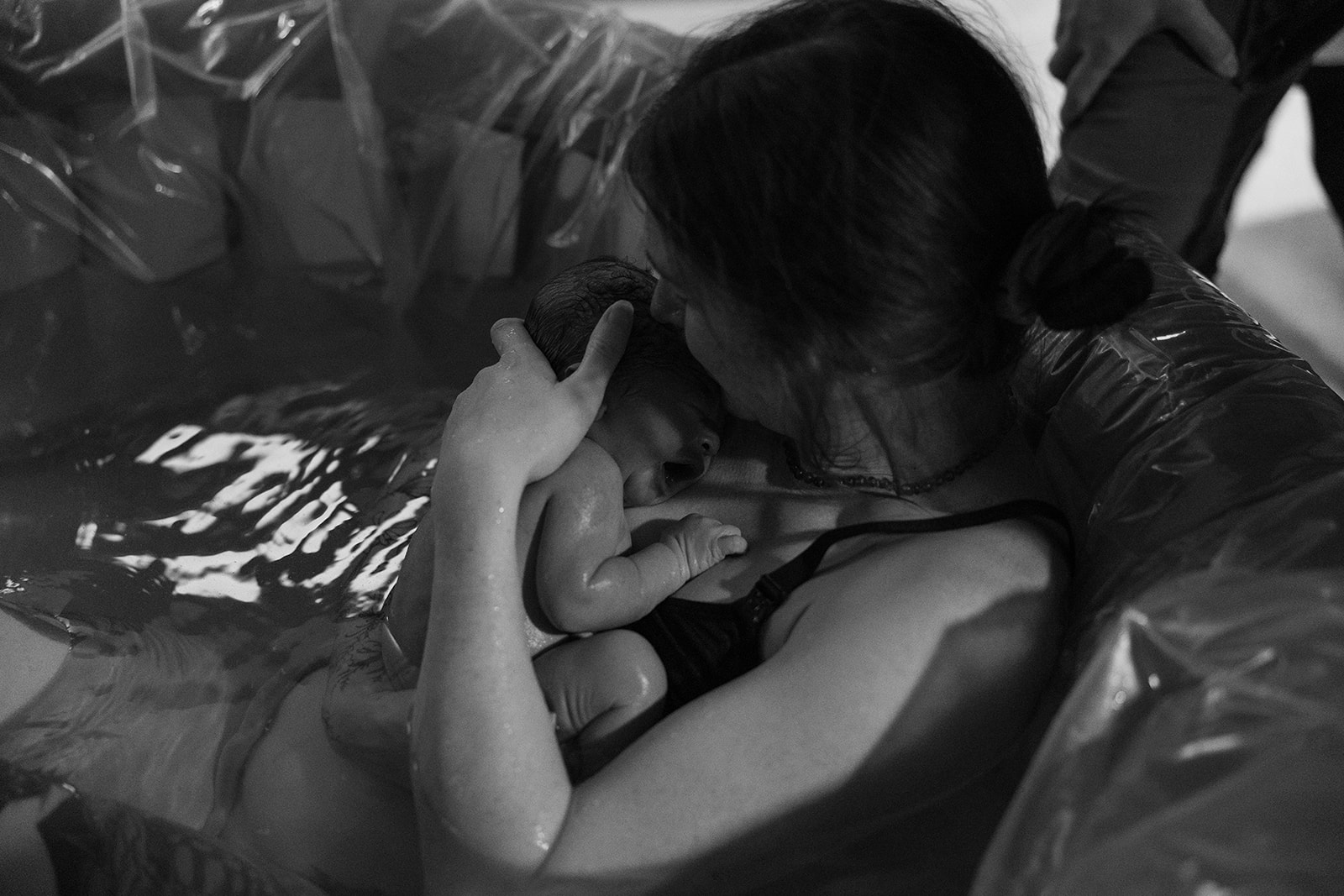 A person holding a newborn baby close, with the baby's head resting on their shoulder, in black and white.