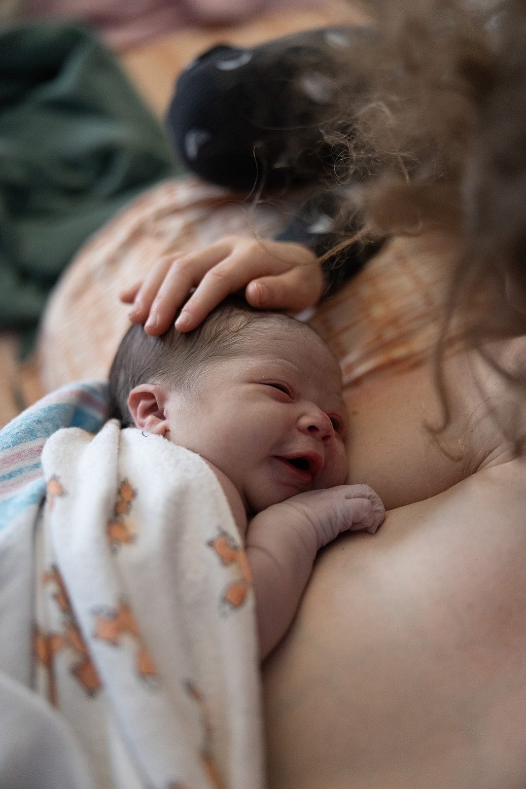 A baby is breastfeeding, with a hand gently resting on the baby's head, and a dog nearby. The scene is intimate and tender.