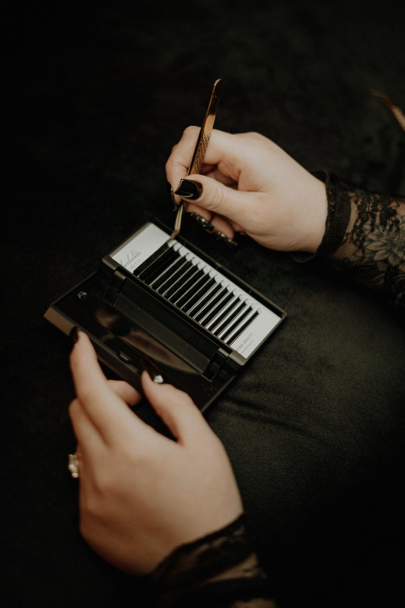 Person holding a miniature piano and a pen, wearing lace sleeves, on a dark surface.