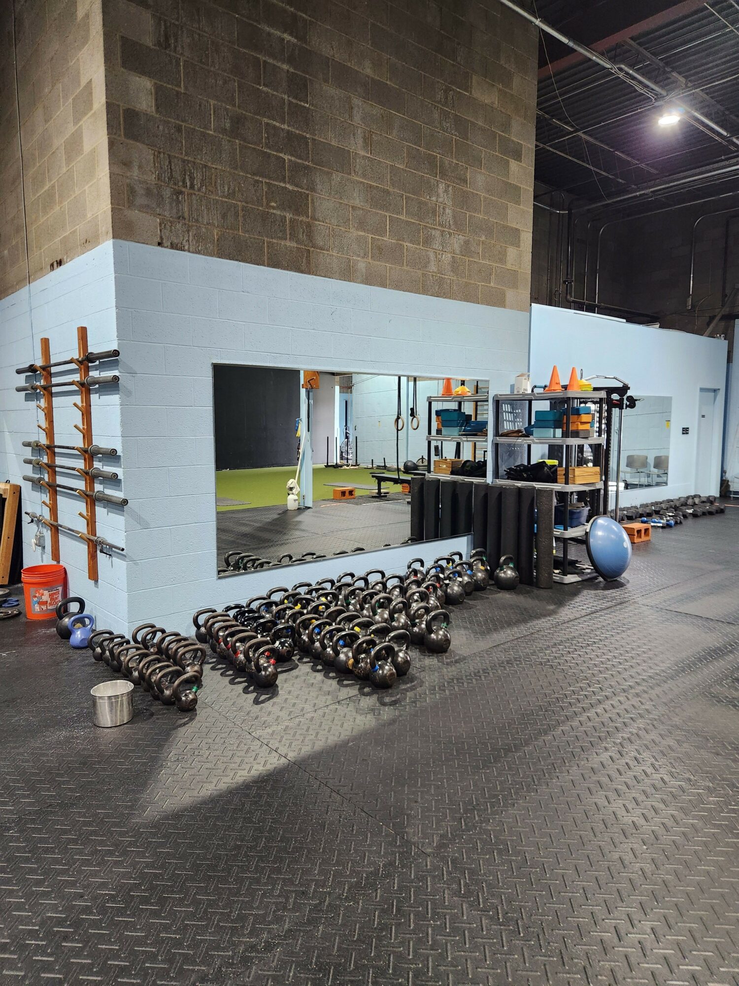 Gym equipment with chains and weights on a gray floor, wall with shelves and workout gear in background.