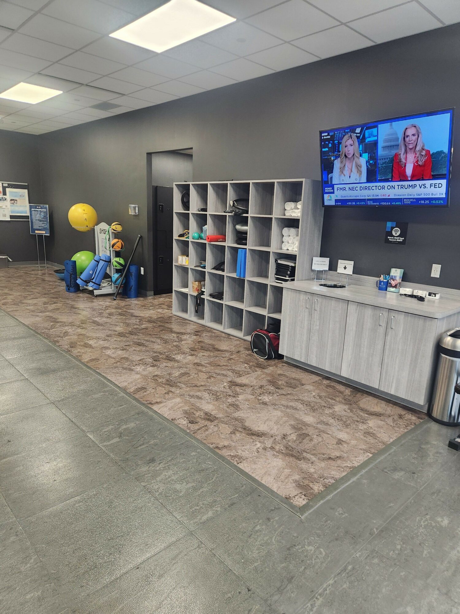 Reception area with a TV, cubby shelves, and a yellow ball, with a gray wall and tiled floor.