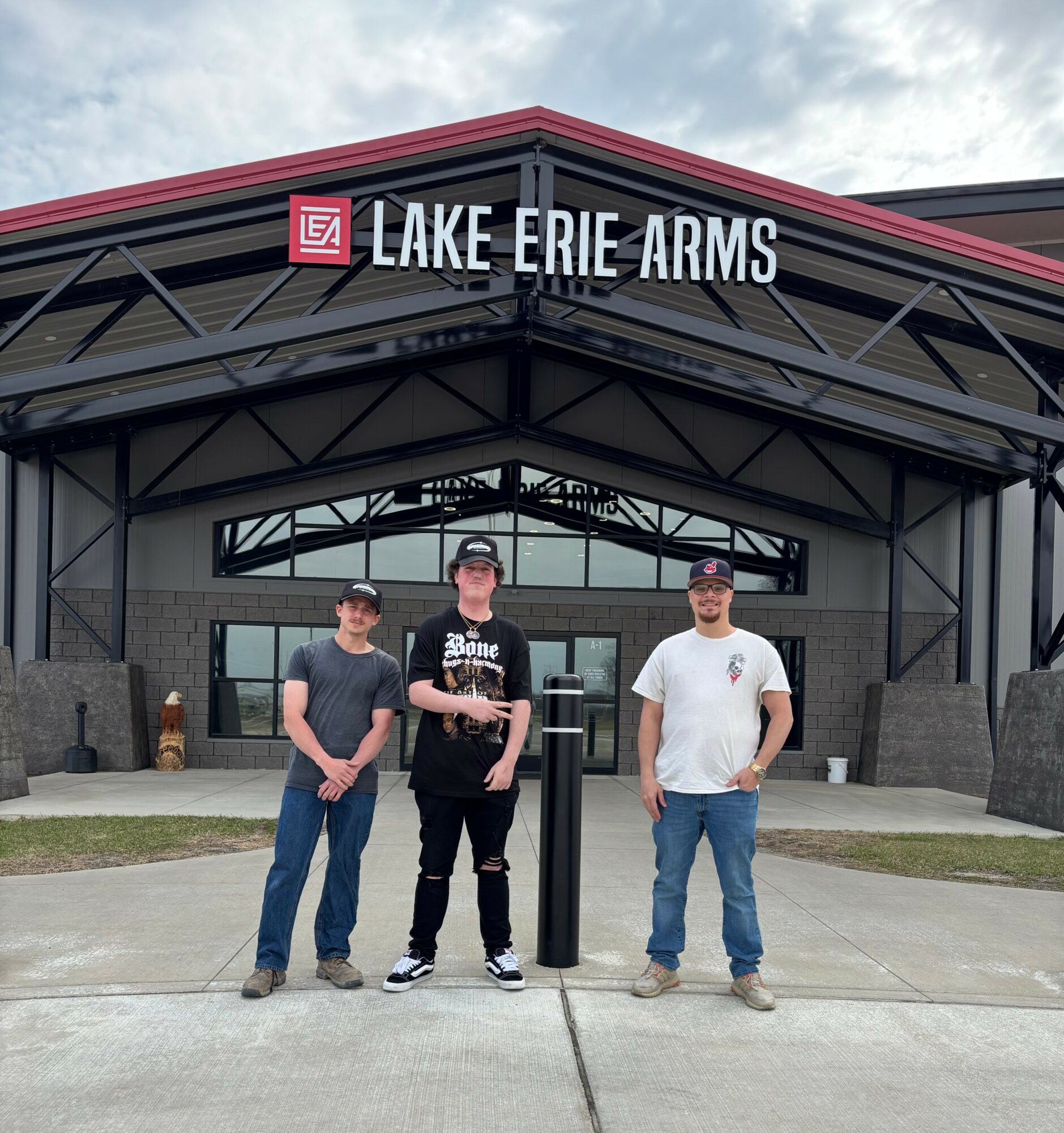 Three people stand in front of a building with a sign that reads 'Lake Erie Arms.'