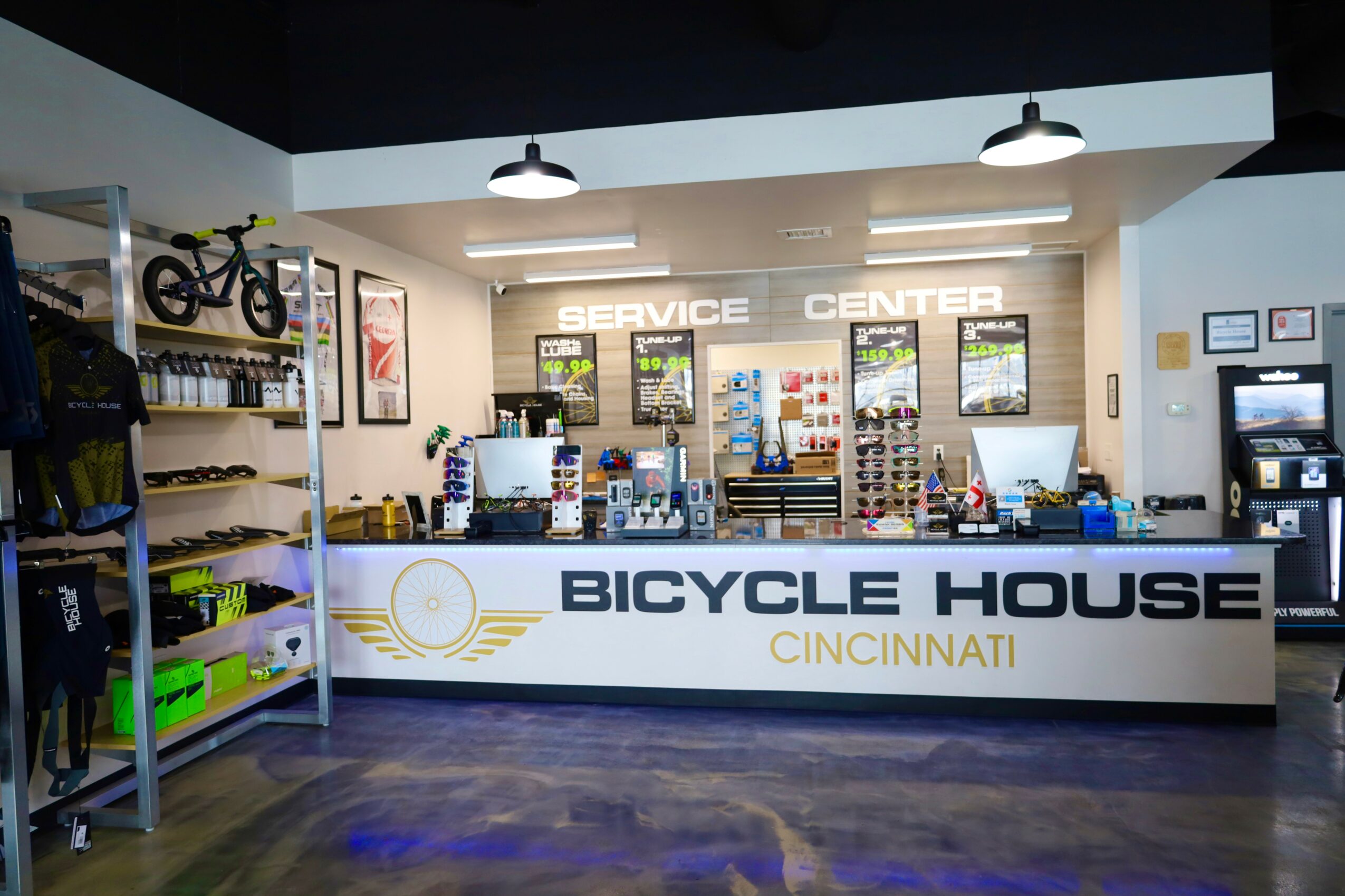 Bike shop counter with shelves of cycling gear and accessories, service center sign, and display area, in a modern store.