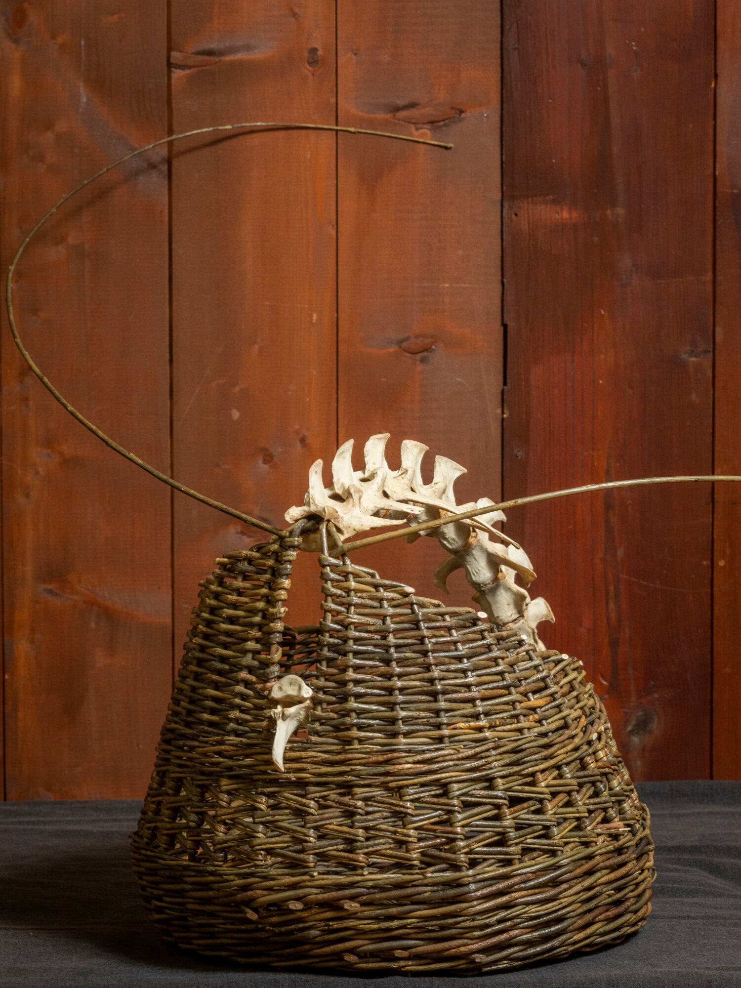 Wicker basket with a white decorative object on top, set against a wooden wall background.